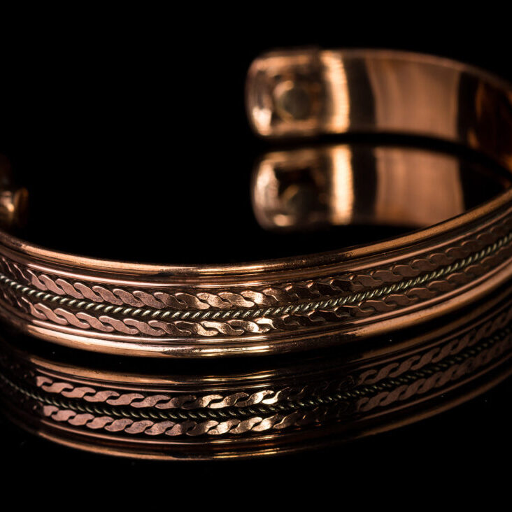 Close up men's copper ornate bracelet isoalted on black background with reflection